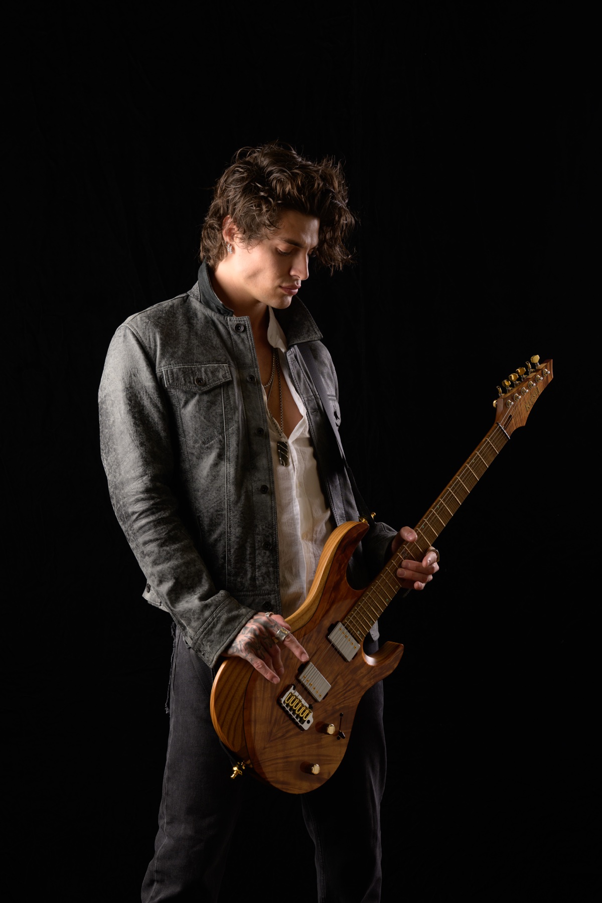 Jon Dretto in a gray jacket holding a guitar in a professional studio portrait